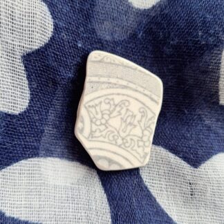 A white and grey sea pottery brooch