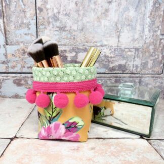 A mini velvet storage pot in a yellow pineapple print and with a cerise pom pom trim.
