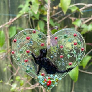 Cat heart hanger with a lovley black cat playing in the garden of flowers. approx 9cm