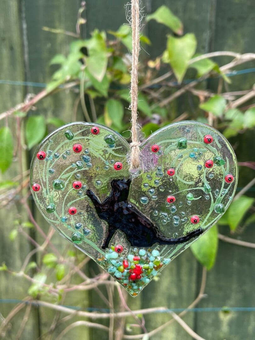 Cat heart hanger with a lovley black cat playing in the garden of flowers. approx 9cm