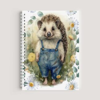 A spiral-bound A5 notebook on a wooden desk featuring a watercolor illustration of a cute hedgehog wearing blue denim dungarees, surrounded by white daisies and green leaves.