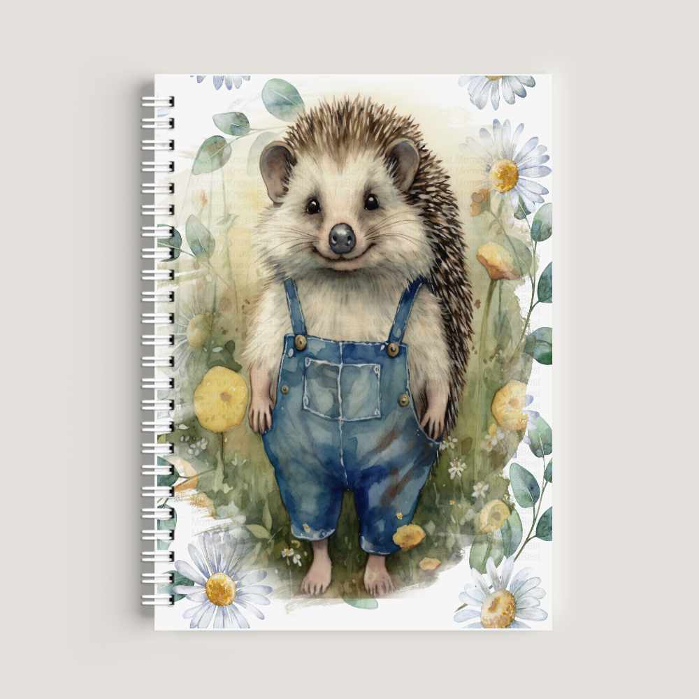 A spiral-bound A5 notebook on a wooden desk featuring a watercolor illustration of a cute hedgehog wearing blue denim dungarees, surrounded by white daisies and green leaves.
