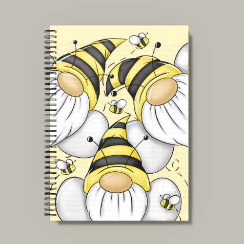 A spiral-bound A5 notebook with a yellow background featuring three gnomes (gonks) wearing yellow and black striped bee hats. Small bumblebees are flying around them. The notebook has black wire binding and is shown on a wooden desk.
