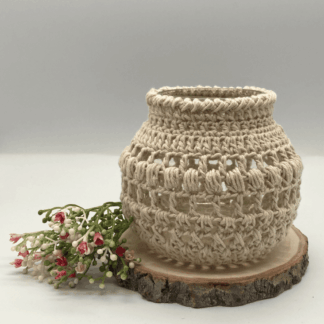 a round globe shaped jar with a cream crochet cover. It's sitting on a slice of wood and on the side are some small flowers