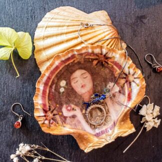 Gilded decoupage scallop shell trinket jewellery dish featuring Klimt's Portrait Of A Woman on a dark table surrounded by jewellery