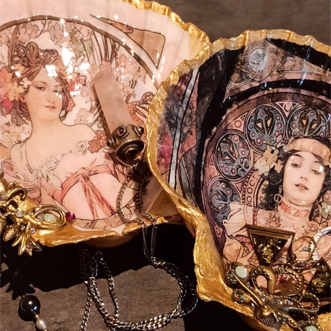 Mucha decoupage gilded extra large scallop shell trinket dishes rest on a dark table surrounded by jewellery