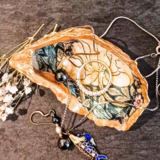 Gilded decoupaged oyster shell trinket dish with William Morris Pimpernel design on a dark table surrounded by jewellery and dried flowers