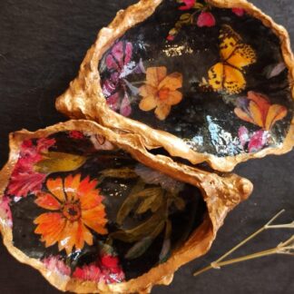 Pair of gilded oyster shells with a vintage, bright floral design on a black background. The shell trinket dishes rest on a dark surface