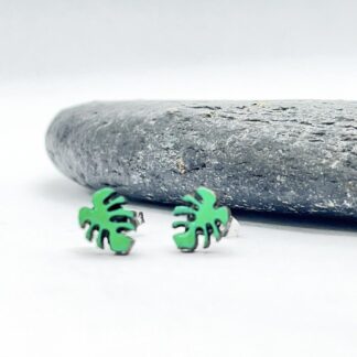 Bright green monstera leaf earrings on a white background in front of a grey slate stone.