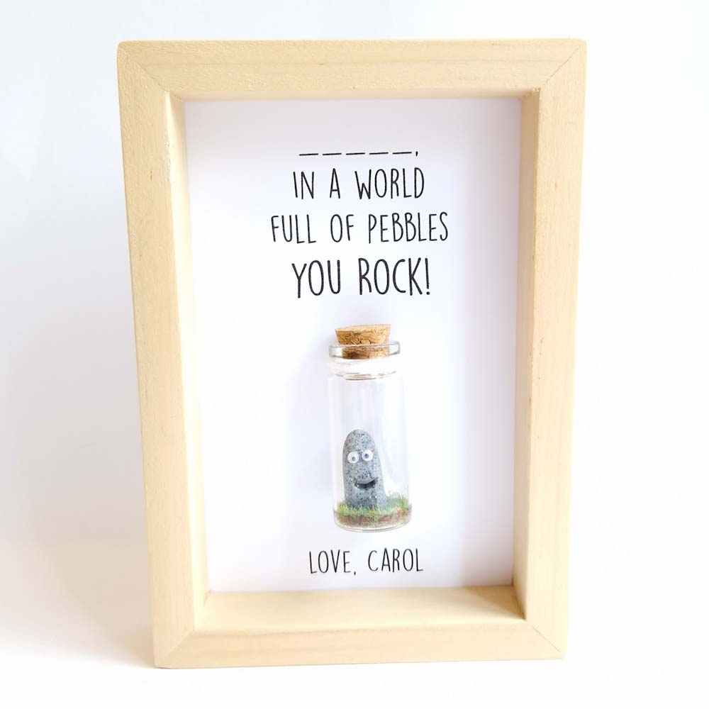 Polymer clay rock figure with googly eyes, enclosed in a miniature glass bottle and framed.