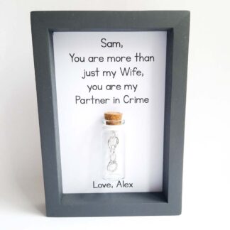 Grey frame with a miniature glass bottle attached inside containing silver handcuffs