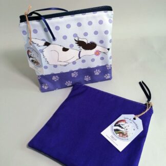 Flat, cotton toiletries bag featuring a zooming dog with a pink flower in its mouth. Various shades of purple and pale blue, spotty background, paw print base and a dark purple back.