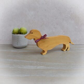 Handcrafted light hardwood Dachshund ornament with tartan ribbon tied around its neck.