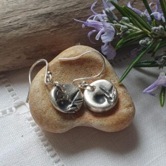 a handmade pair of dainty silver drop earrings, small discs of silver with a herb imprint in black finish.