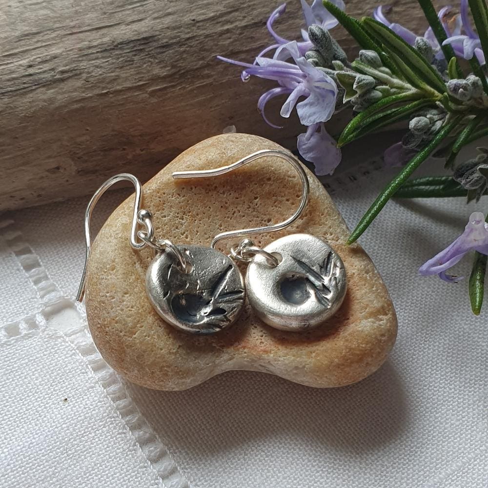 a handmade pair of dainty silver drop earrings, small discs of silver with a herb imprint in black finish.