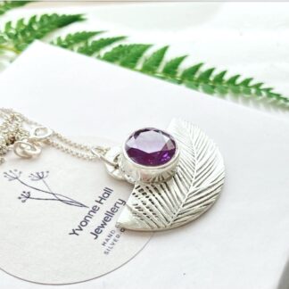 Half moon shaped fine silver necklace with a large 10mm. amethyst coloured cubic zirconia displayed on a white gift box.