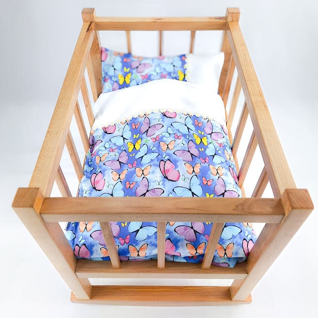 Traditionally built frame of wooden dolls cot with pillow and duvet
