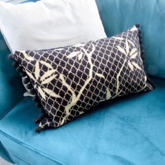 A black velvet boudoir style cushion with a black pompom trim