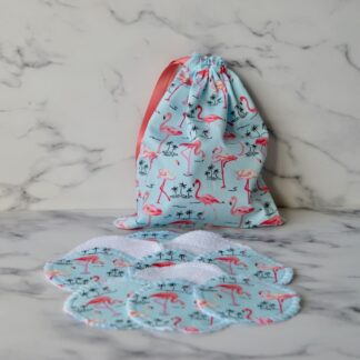Set of cotton pads with a matching storage bag. Fabric is light blue with pink flamingos. The bag is closed with a dusky pink ribbon drawstring.