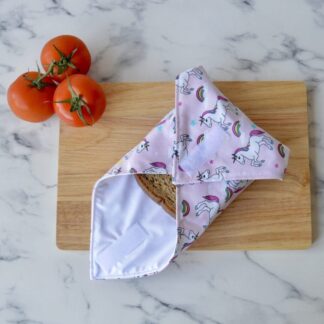 Light pink unicorn sandwich wrap on a wooden chopping board. Wrap is folded up with a sandwich inside