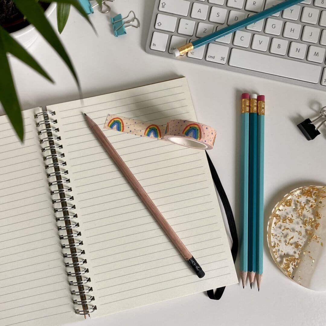 Image shows a desk with keyboard, accessories and an open notebook with wash tape & sharpened HB pencil