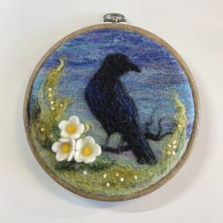 Handcrafted needle-felted crow silhouette in a hoop, featuring wildflowers and a serene nature-inspired background.