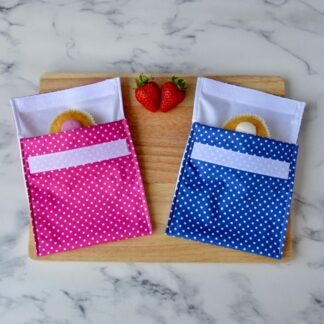 Pink and blue polka dot snack bags on a wooden board with cupcakes inside and fresh strawberries placed around them.