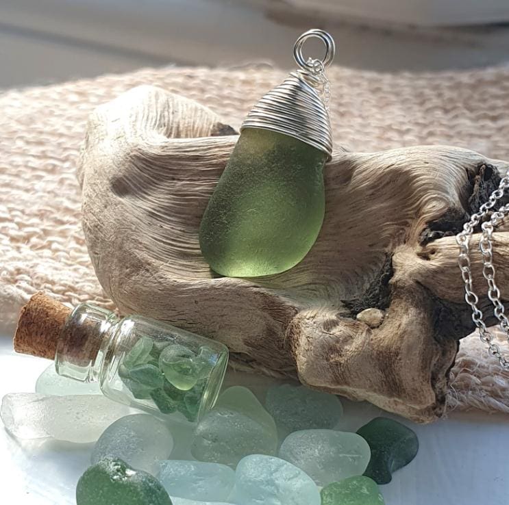 Seafoam green seaglass bean with a silver wire wrapped top resting on some drift