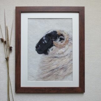A Scottish Blackface sheep created with wool. The sheep is facing towards the left and is head and shoulders only. The frame is dark brown and has a cream coloured mount.