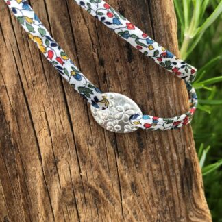 A silver oval bracelet with flower print and adjustable Liberty fabric cord