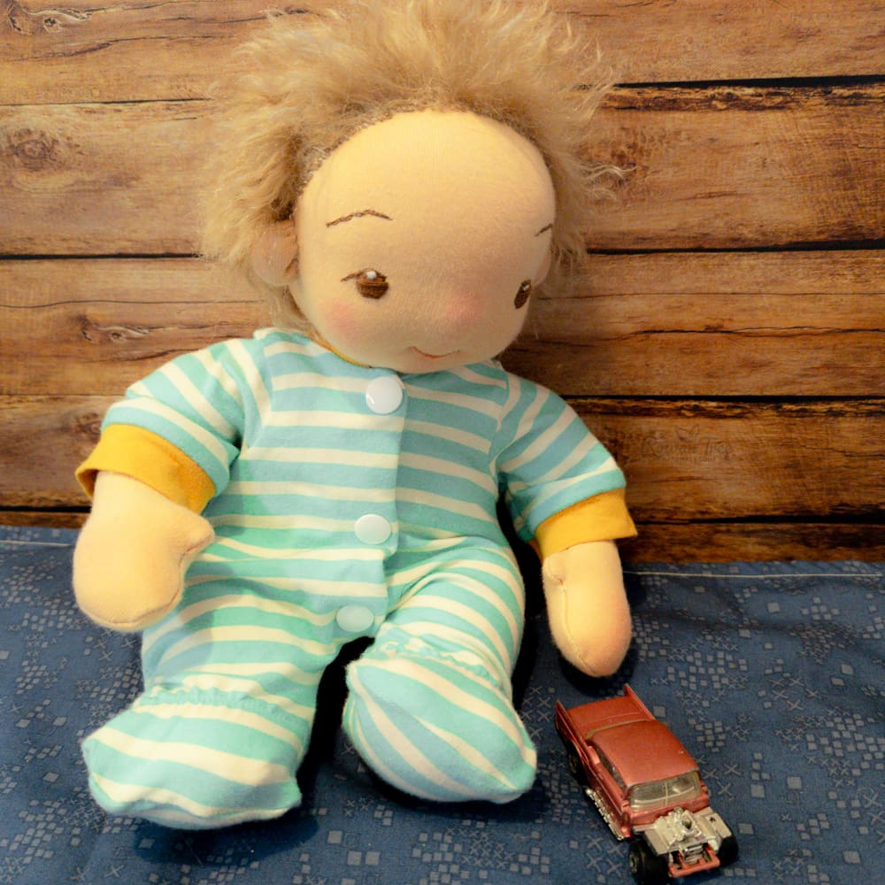 handmade fabric baby doll with brown hair and brown eyes dressed in a stripy onesie with his hand on an vintage toy car