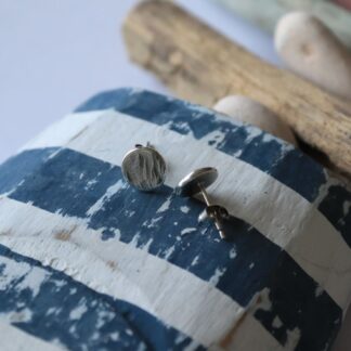 Recycled silver round stud earrings, textured with bark and finished with silver stud backs. Displayed here on blue and white driftwood.