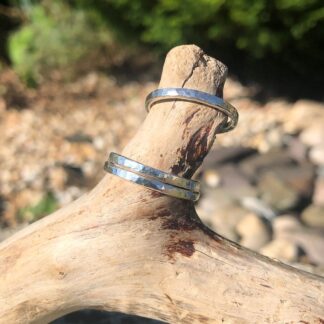 Three silver hammered rings displayed on a piece of driftwood, showcasing their hammered textured surface