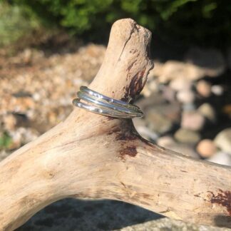 Three silver hammered rings displayed on a piece of driftwood, showcasing their hammered textured surface