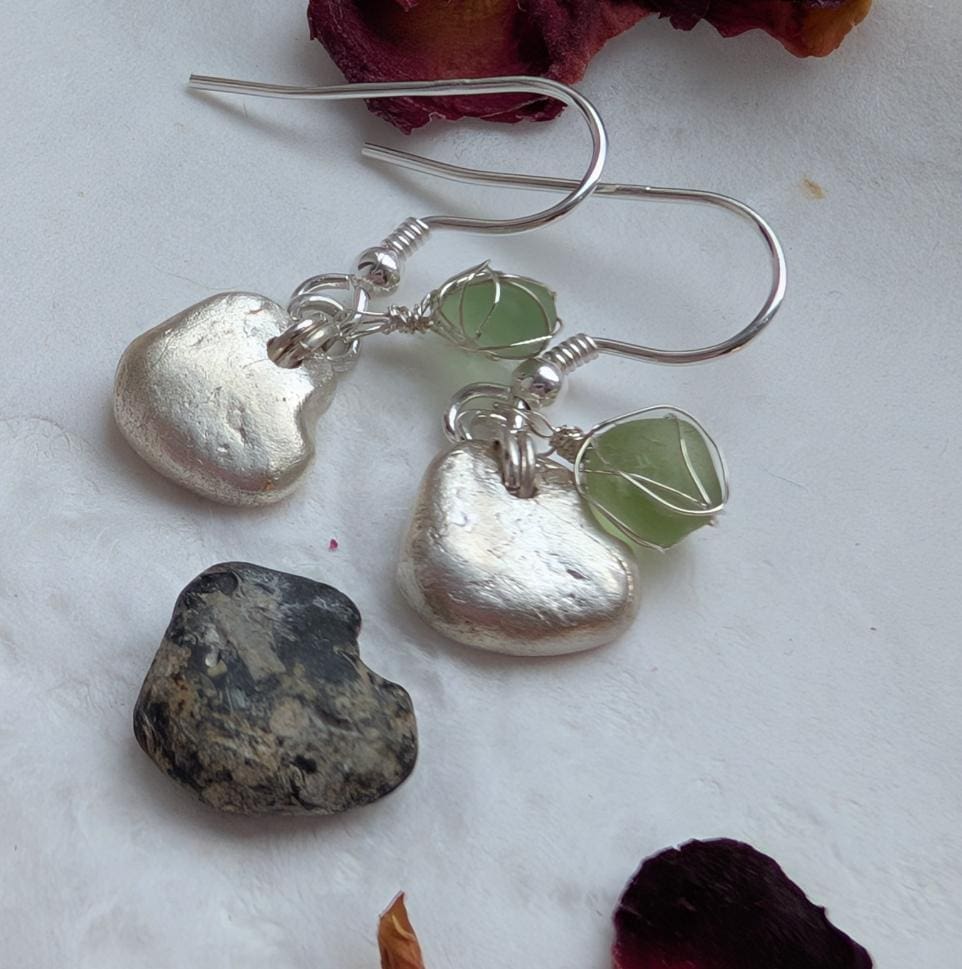 A pair of dainty silver heart earrings each with a tiny piece of pale green sea glass wrapped in very fine silver wire