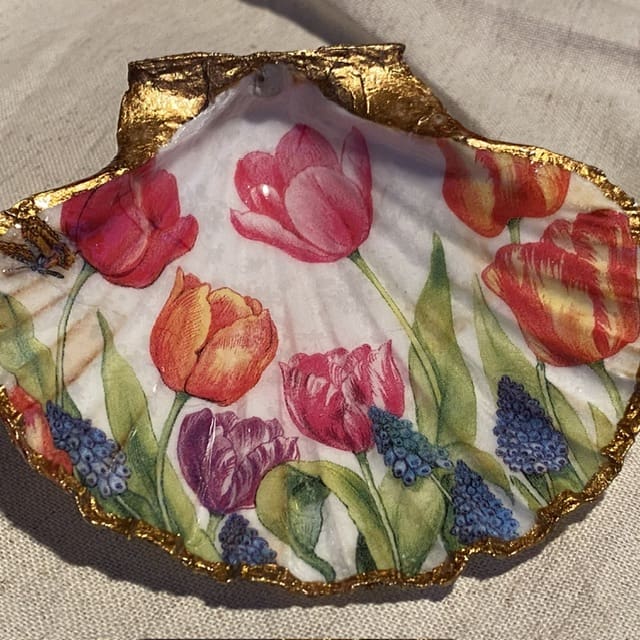 A handmade decoupaged scallop shell with tulips, muscari and green leaves.