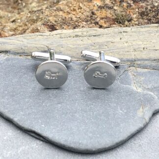 Round silver cufflinks, one featuring a dog and the other featuring a bone.