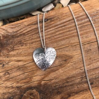 Silver heart-shaped necklace with embossed floral print and a patina.