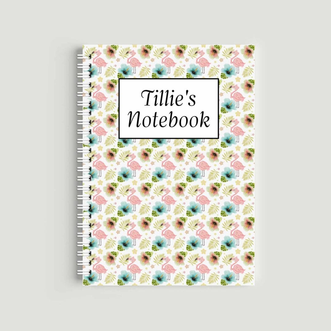 A spiral-bound A5 notebook with a repeating pattern of pink flamingos, blue hibiscus flowers, and palm leaves. A central white box with a black border reads "Tillie's Notebook" in a classic script font.