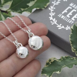11.5mm and 14mm diameter argentium sterling silver round pebble pendants with front facing u-shaped bail and double jump rings on sterling silver mini belcher chains shown on hand for size reference