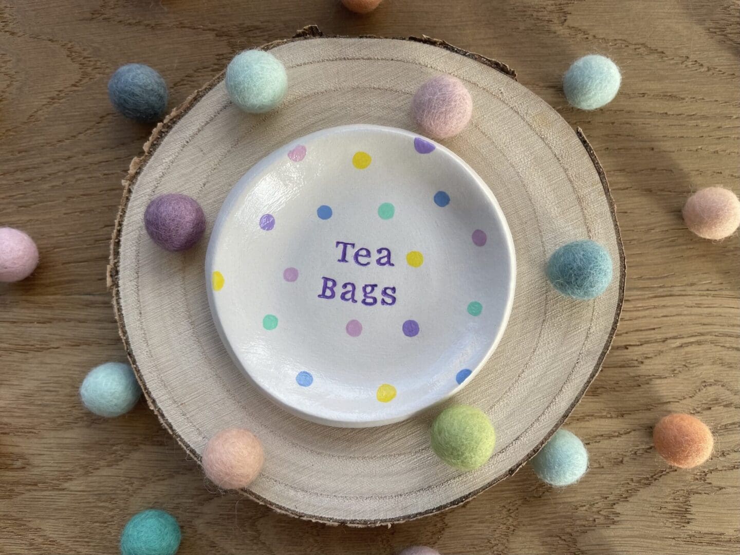 Multi coloured polka dot Tea Bag Dish surrounded by colourful felt balls