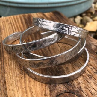 Sustainable textured silver cuff bangles stacked on driftwood, highlighting their coastal inspiration.
