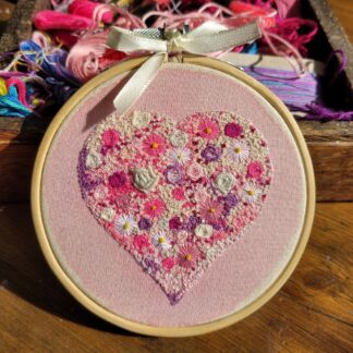 Pink hand embroidered flowers in a heart shape presented in a 4 inch hoop to hang on your wall.