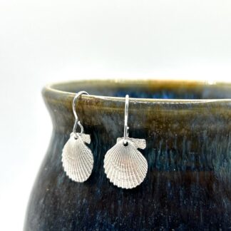 silver scallop shell earrings hanging from the side of an earthenware mug
