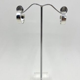 A small pair of sterling silver earrings, displayed on a stand with a white background. The earrings have a post and scroll fitting and a polished mirror finish.