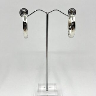 Handmade sterling silver hoop earrings with post and scroll fittings for the earlobe. Displayed on a stand against a white background.