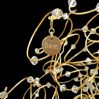 A 9mm gold disc charm engraved with the name Sam. The charm is wired to hang off a branch of a Maisie M Tree wedding cake topper tree.
