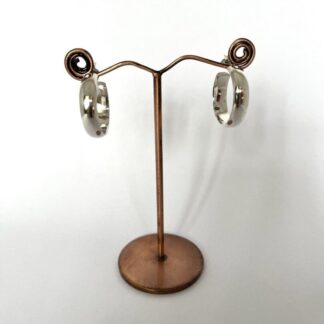 A pair of chunky sterling silver hoop earrings displayed on a stand with a white background. The earrings are handmade and have post and scroll fittings
