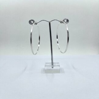 A pair of large handmade silver hoop earrings displayed on an earring stand against a white background