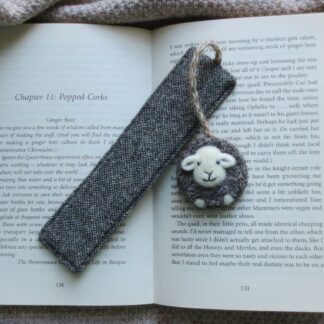 The bookmark is laying across an open book and the book is placed on a wool blanket.